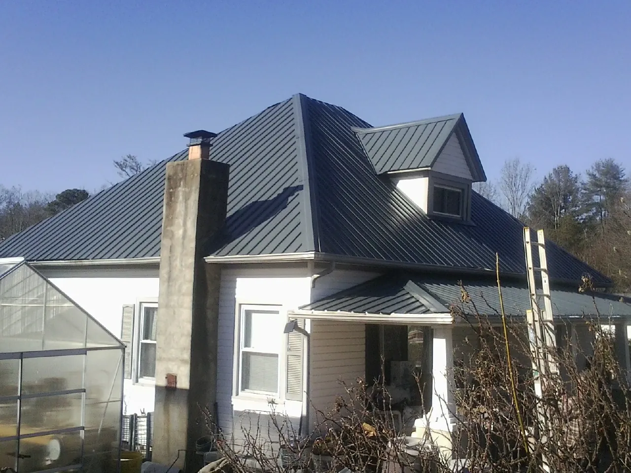 Dark blue standing seam metal roof on a white farmhouse with dormer — Slate & Tile Roof Repair by Roofing Brothers in Lattimore