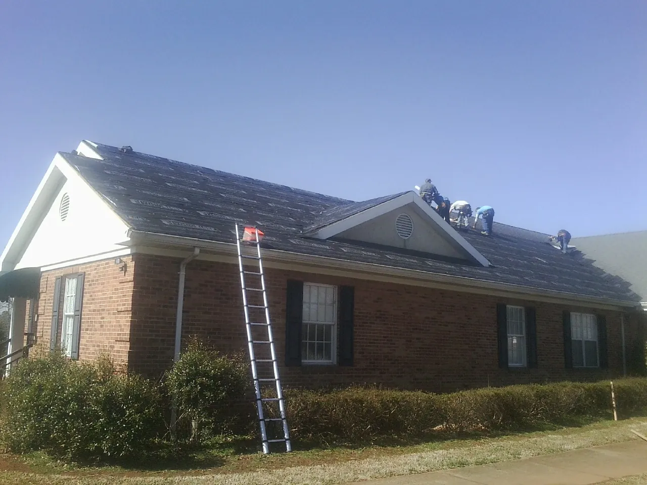 Crew tearing shingles off a brick ranch roof with a ladder set — Emergency Roof Repair work by our crew in Lattimore