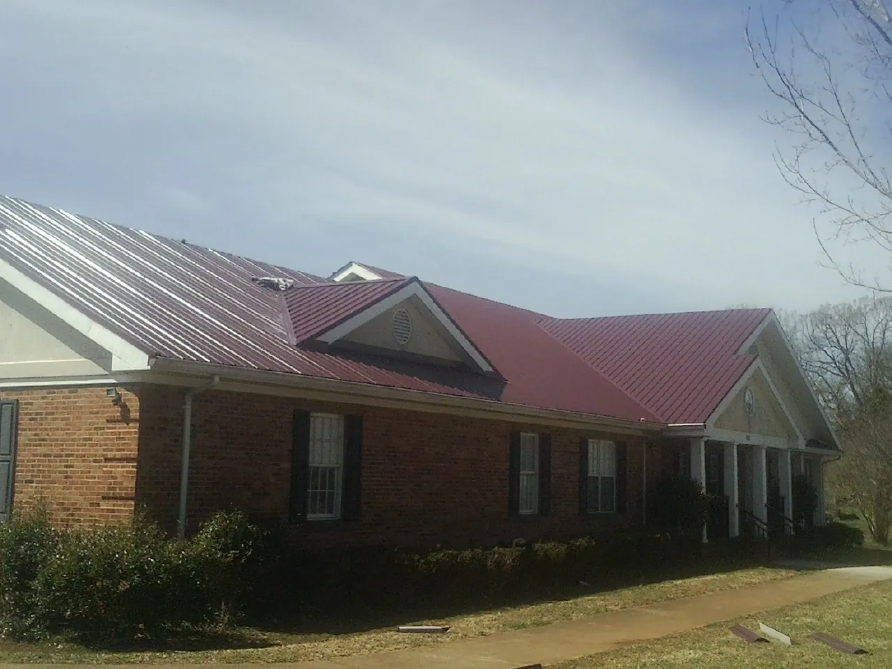 Red metal roof with gabled entries on a long brick building, from a Hail Damage Roof Repair job in Lattimore