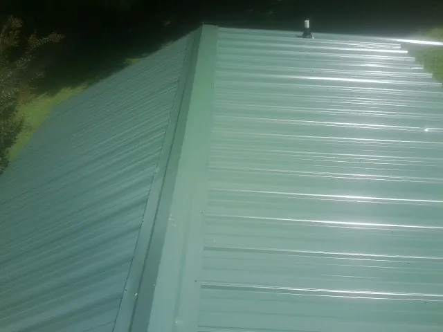 New green metal panels meeting at the ridge of a roof — Flat Roof Repair work by our crew in Lattimore