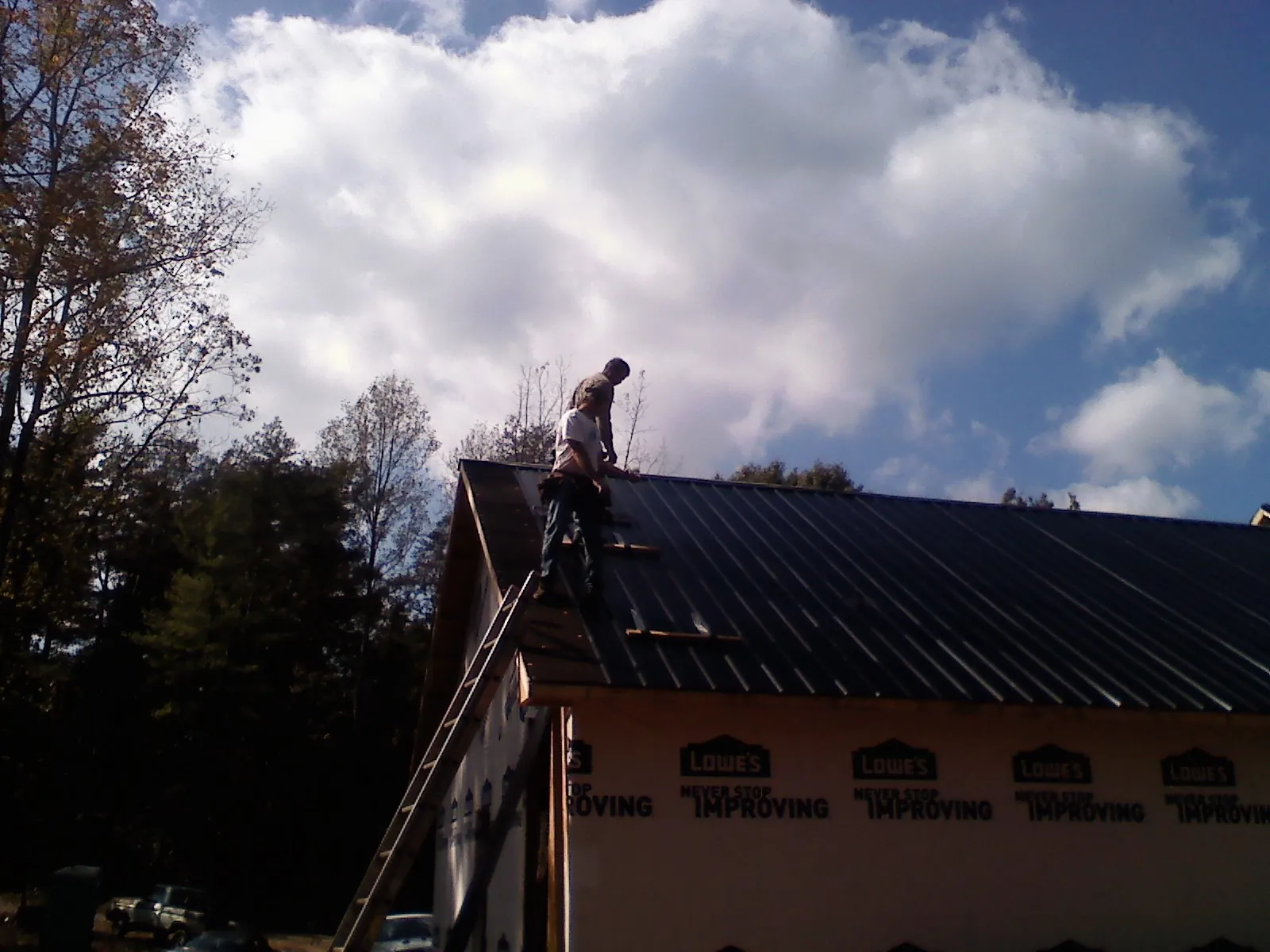Roofer fastening dark metal panels high against a cloudy sky, from a Roof Inspection job in Lattimore