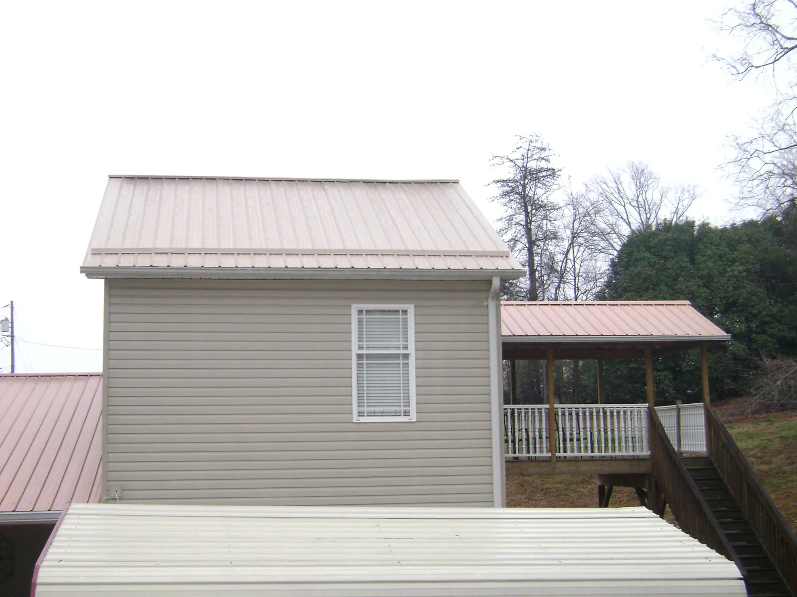 Tan metal roofs on a two story addition and attached porch, from a Roof Replacement job in Lattimore